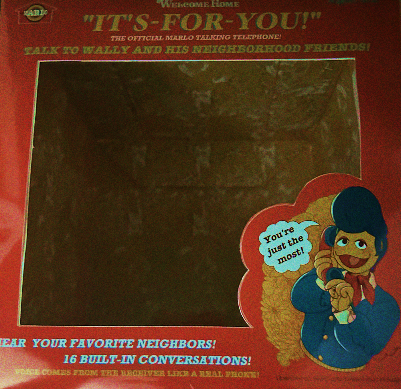 A photograph showing the front of the box, which reads reads: 'Welcome Home IT'S-FOR-YOU! The official Marlo Talking Telephone! Talk to Wally and his neighborhood friends! Hear your favorite neighbors! 16 built-in conversations! Voice comes from the receiver like a real phone!' Alongside an illustration of Wally on the phone, twirling the cord and smiling, saying 'You're just the most!'